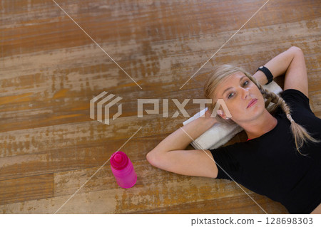 Woman relaxing on wooden floor with towel and water bottle after workout Woman relaxing on wooden floor with towel and water bottle after workout 128698303