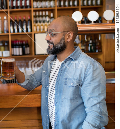 Man enjoying cold beer at lively bar with wooden shelves and bottles 128698304