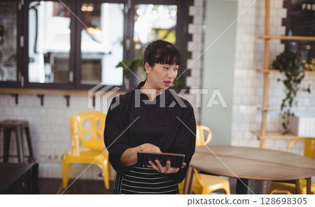 Chef in modern cafe using digital tablet, planning menu with focused expression 128698305