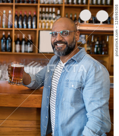 Smiling man enjoying beer at bar with shelves of bottles in background 128698308
