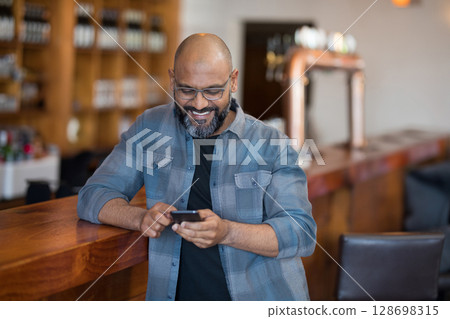 Man using smartphone at bar, enjoying relaxed atmosphere and smiling 128698315