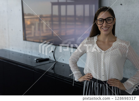 Smiling woman wearing glasses in modern office environment, feeling confident, copy space 128698317