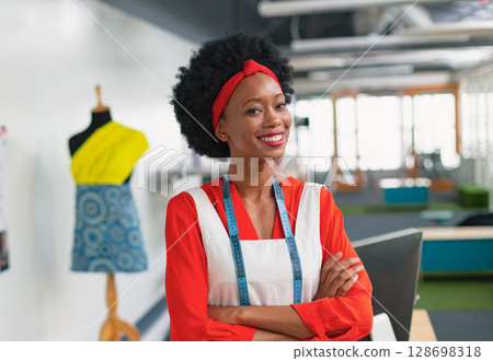 Fashion designer smiling confidently in studio with mannequin and measuring tape 128698318