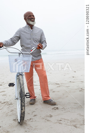 Smiling man standing with bicycle on beach, enjoying peaceful day Smiling man standing with bicycle on beach, enjoying peaceful day 128698321