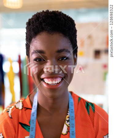 Smiling fashion designer wearing vibrant dress with measuring tape in studio Smiling fashion designer wearing vibrant dress with measuring tape in studio 128698322