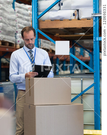 Warehouse manager checking inventory with clipboard, focusing on stacked boxes Warehouse manager checking inventory with clipboard, focusing on stacked boxes 128698331