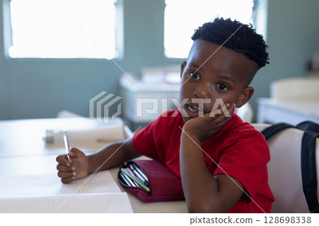 In school, young boy in red shirt daydreaming during class at desk 128698338