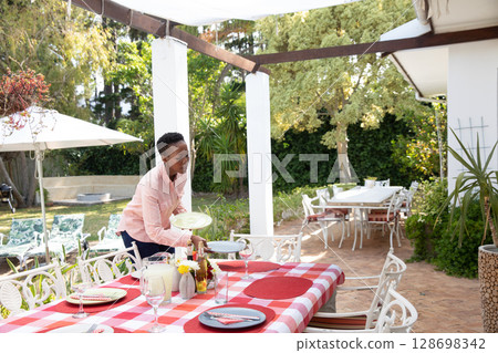 Setting outdoor table with plates, African American woman preparing for family meal Setting outdoor table with plates, African American woman preparing for family meal 128698342
