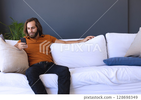 Relaxing on sofa, man using smartphone at home, enjoying leisure time, copy space Relaxing on sofa, man using smartphone at home, enjoying leisure time, copy space 128698349
