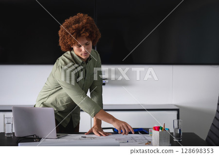 Business professional reviewing documents at office desk with laptop and glasses 128698353
