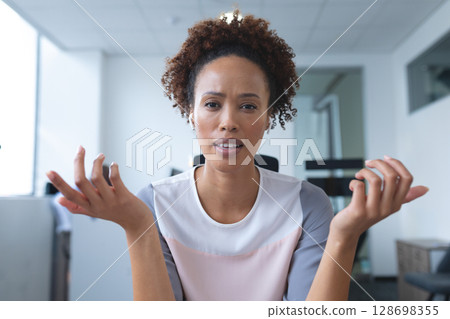 Confused businesswoman gesturing during video call in modern office setting 128698355