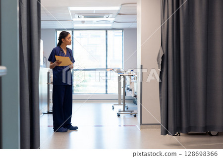 Nurse in hospital corridor holding patient files, preparing for rounds, copy space 128698366