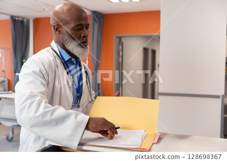 Doctor reviewing patient files at hospital nurses' station, focused on work, copy space 128698367