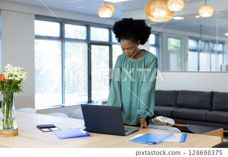 Businesswoman focusing on laptop work in modern office with documents nearby, copy space 128698375