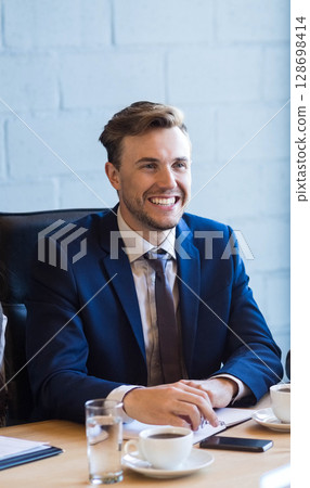 Smiling businessman in suit attending meeting with coffee and documents 128698414
