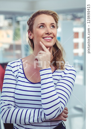 Smiling businesswoman in striped shirt thinking creatively in modern office Smiling businesswoman in striped shirt thinking creatively in modern office 128698415