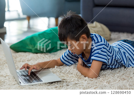 Young boy using laptop on carpet at home, focused on screen Young boy using laptop on carpet at home, focused on screen 128698450