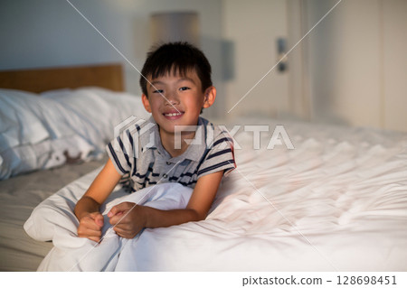 Smiling boy relaxing on bed at home, enjoying cozy morning light, copy space 128698451