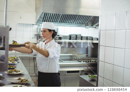 Chef plating dishes in professional kitchen, focused on presentation and quality Chef plating dishes in professional kitchen, focused on presentation and quality 128698454