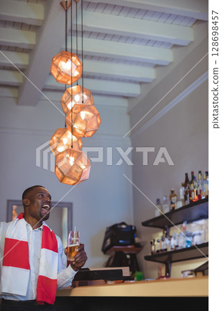 Man enjoying drink at bar, wearing scarf, smiling under modern pendant lights, copy space 128698457