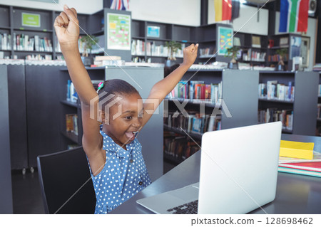 In school library, girl celebrating success using laptop, feeling excited In school library, girl celebrating success using laptop, feeling excited 128698462