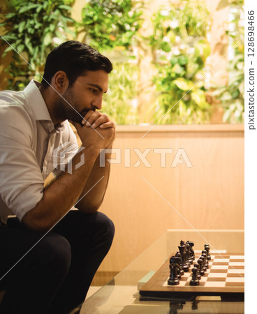 Man concentrating on chess game in modern office with green plants, copy space 128698466