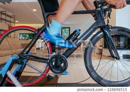 A triathlete riding a triathlon bike on a machine simulation in a modern living room. Training during pandemic conditions. 128698513