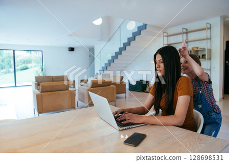 Mother with her daughter talking on laptop with family and friends while sitting in modern living room of big house. 128698531