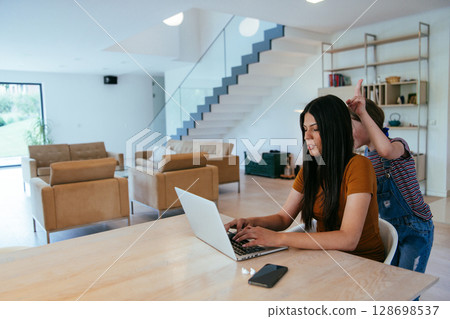 Mother with her daughter talking on laptop with family and friends while sitting in modern living room of big house. 128698537