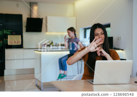 Mother with her daughter talking on laptop with family and friends while sitting in modern living room of big house. 128698548