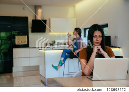 Mother with her daughter talking on laptop with family and friends while sitting in modern living room of big house. 128698552
