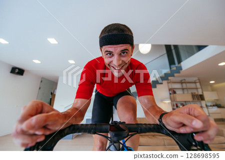 A triathlete riding a triathlon bike on a machine simulation in a modern living room. Training during pandemic conditions. 128698595