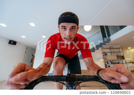 A triathlete riding a triathlon bike on a machine simulation in a modern living room. Training during pandemic conditions. 128698601