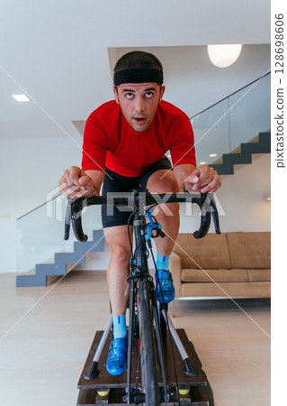 A triathlete riding a triathlon bike on a machine simulation in a modern living room. Training during pandemic conditions. 128698606