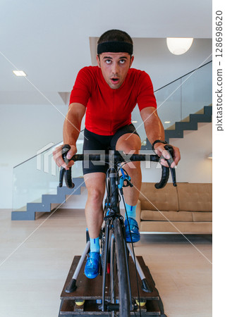 A triathlete riding a triathlon bike on a machine simulation in a modern living room. Training during pandemic conditions. 128698620