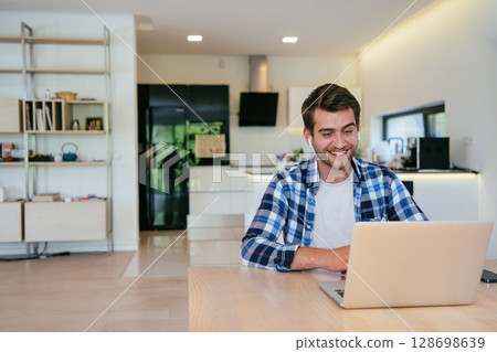 A freelancer sitting at a table in a modern living room, with headphones using a laptop for business video chat, conversation with friends and entertainment 128698639