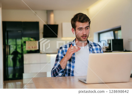 A freelancer sitting at a table in a modern living room, with headphones using a laptop for business video chat, conversation with friends and entertainment A freelancer sitting at a table in a modern living room, with headphones using a laptop for business video chat, conversation with friends and entertainment 128698642