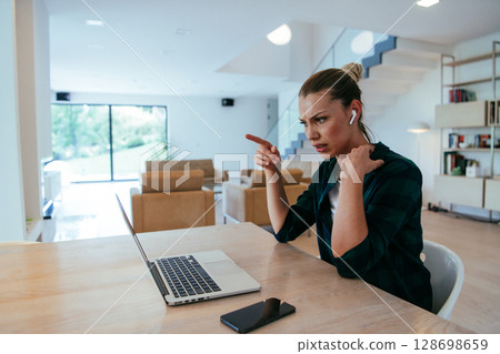 Woman sitting in living room using laptop looking at cam talk by video call with business friend relatives, head shot. Job interview answering questions Woman sitting in living room using laptop looking at cam talk by video call with business friend relatives, head shot. Job interview answering questions 128698659