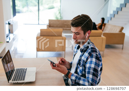 A freelancer sitting at a table in a modern living room, with headphones using a laptop for business video chat, conversation with friends and entertainment 128698707
