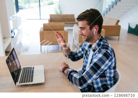 A freelancer sitting at a table in a modern living room, with headphones using a laptop for business video chat, conversation with friends and entertainment 128698710