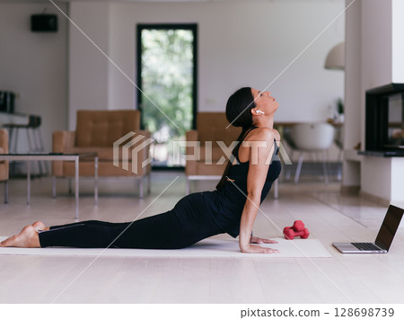 Young Beautiful Female Exercising, Stretching and Practising Yoga with Trainer via Video Call Conference in Bright Sunny House. Healthy Lifestyle, Wellbeing and Mindfulness Concept. 128698739