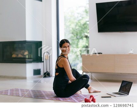 Young Beautiful Female Exercising, Stretching and Practising Yoga with Trainer via Video Call Conference in Bright Sunny House. Healthy Lifestyle, Wellbeing and Mindfulness Concept 128698741