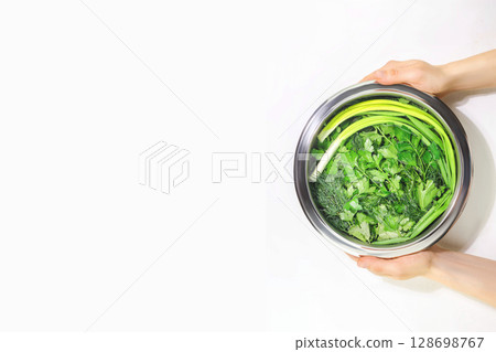 Woman's hands hold bowl with salad greenery. Parsley, dill, cilantro, green onion in bowl on white background. Fresh homegrown greenery. Summer season food. Vegan and vegetarian diet. Copy space 128698767