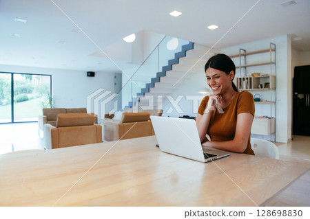 Woman sitting in living room using laptop looking at cam talk by video call with business friend relatives, head shot. Job interview answering questions Woman sitting in living room using laptop looking at cam talk by video call with business friend relatives, head shot. Job interview answering questions 128698830