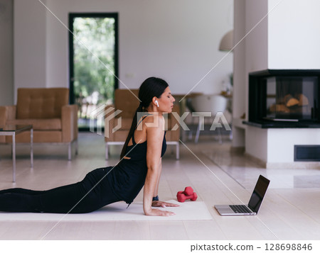 Young Beautiful Female Exercising, Stretching and Practising Yoga with Trainer via Video Call Conference in Bright Sunny House. Healthy Lifestyle, Wellbeing and Mindfulness Concept. 128698846