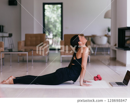 Young Beautiful Female Exercising, Stretching and Practising Yoga with Trainer via Video Call Conference in Bright Sunny House. Healthy Lifestyle, Wellbeing and Mindfulness Concept. 128698847