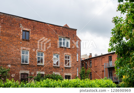 Old red brick residential buildings with overgrown garden and cloudy sky in Europe 128698969