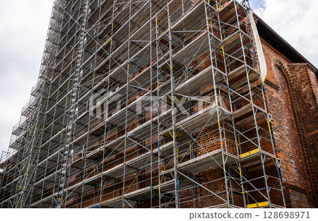 Metal scaffolding covering brick wall of historic building under renovation 128698971