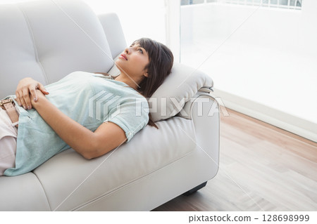 Reclining woman looking upward on leather sofa in living room, with headrest pillow Reclining woman looking upward on leather sofa in living room, with headrest pillow 128698999