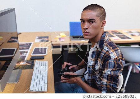 Editing man sitting at wooden desk in studio workspace, with DSLR camera and photos, copy space 128699023